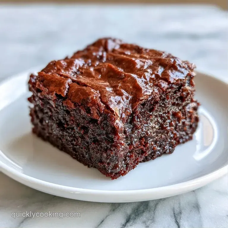 A single square of dark chocolate cake dusted with powdered sugar on a white plate with a side of fresh raspberries.